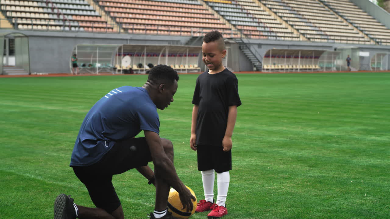 Diverse Trainer and Child Speaking on Football Field Zoom in View of Black Male Coach Explaining Game Strategy to Mixed Race Boy during Football Training on Stadium