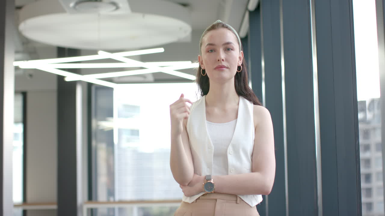 Confident businesswoman standing in modern office, wearing white vest and watch