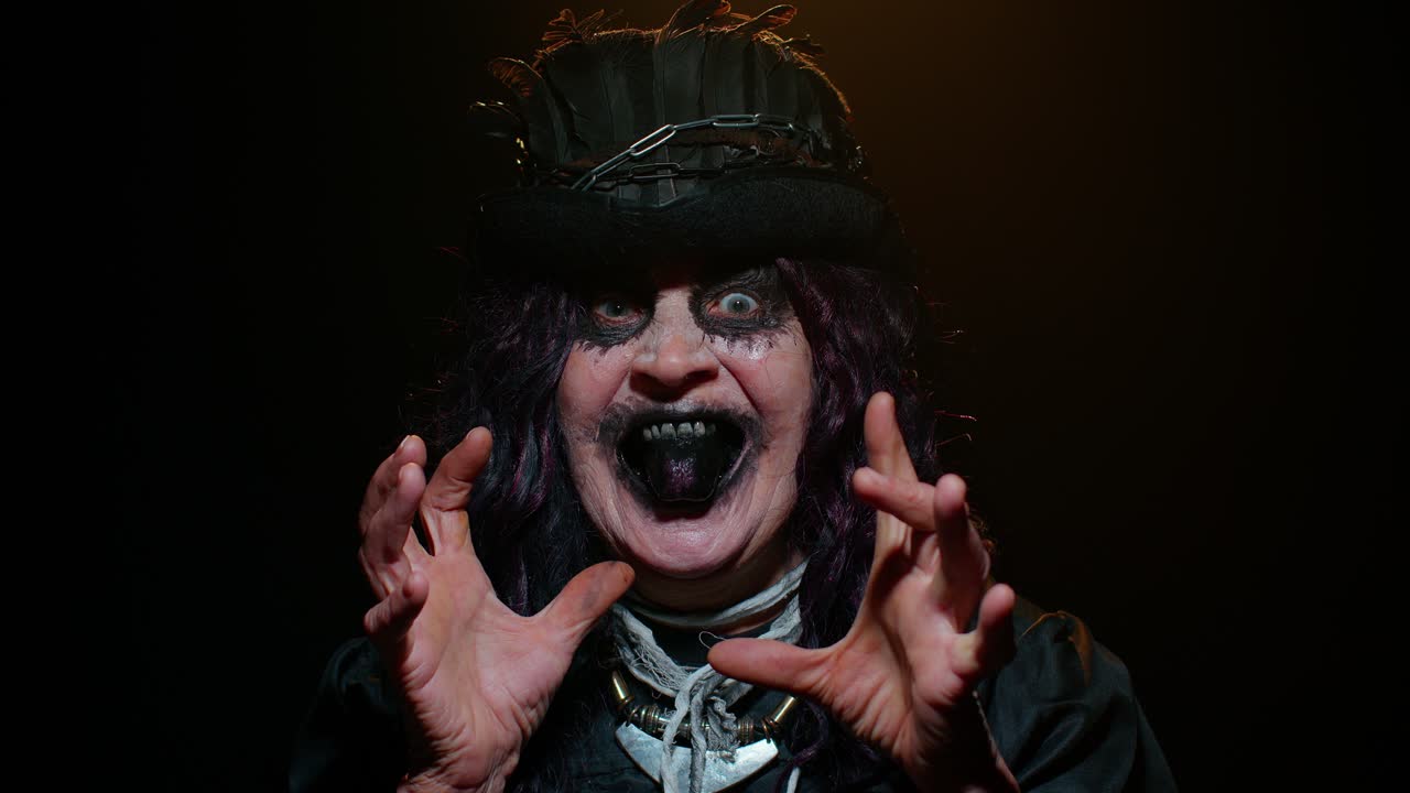 끔찍하고 무서운 할로윈 마녀 메이크업 의상을 입은 사악한 여성이 두려워하려고 얼굴을 만들고 있습니다.