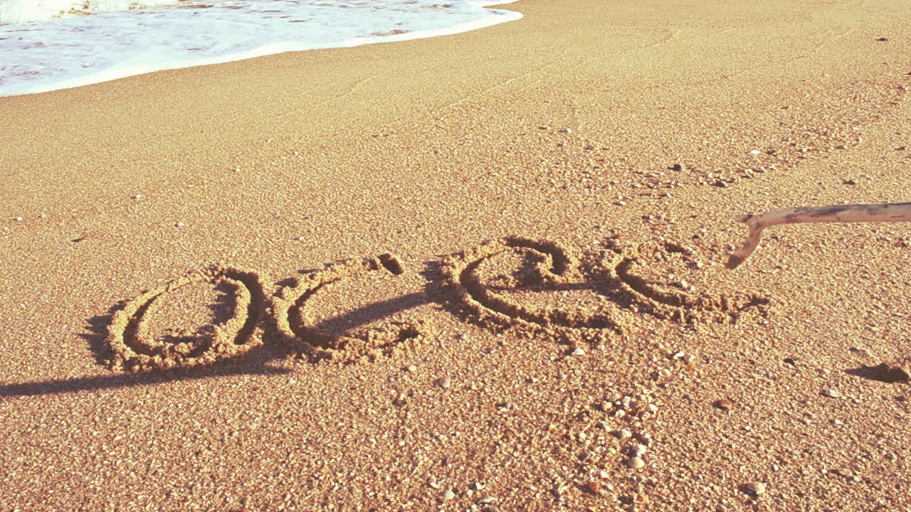 Scriviamo parole sulla sabbia. La parola 'oceano' sulla sabbia. Riprese sulla spiaggia.