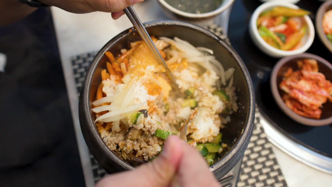 Gambar dari atas seseorang yang sedang mengaduk bibimbap tradisional Korea dalam mangkuk batu dolsot yang mengepul