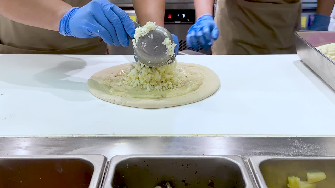 Queijo sendo espalhado na massa de pizza por chefs