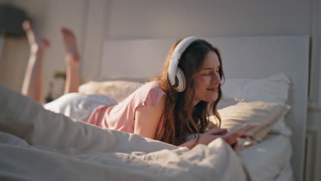 relaxed female listening music at home morning. carefree young woman resting bed