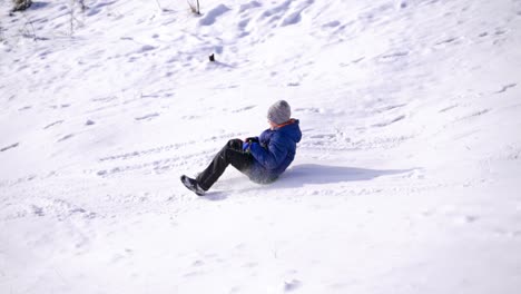 child boy having fun, riding from a hill. frost winter season.cute little boy with saucer sleds outdoors on winter day and hits his friend or sister or brother, ride down the hills, winter games and fun. two children hit while sledging.