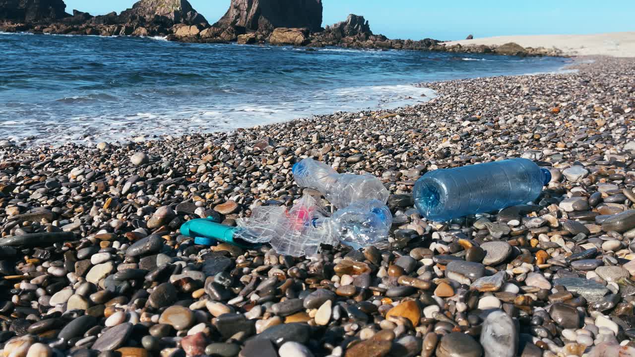 Bottiglie di plastica e spazzatura portate a riva su una spiaggia rocciosa, evidenziando l'inquinamento costiero