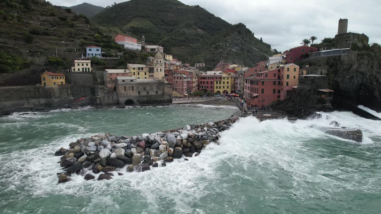 Zoom indietro, ripresa aerea con drone del borgo italiano delle Cinque Terre vicino alla spiaggia con le onde che si infrangono.
