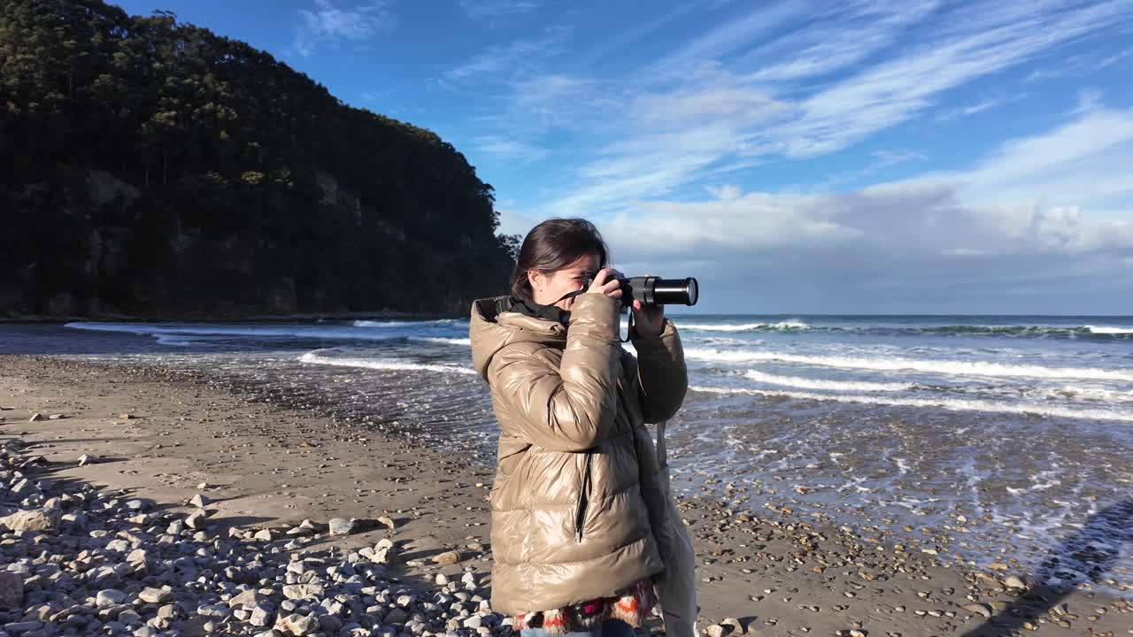 Plano geral de mulher fotografando ondas em uma bela praia costeira