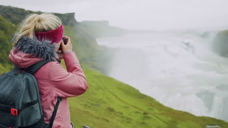 una turista con una mochila captura la cascada de gullfoss con su cámara. fama atracción y destino histórico en islandia en el círculo dorado
