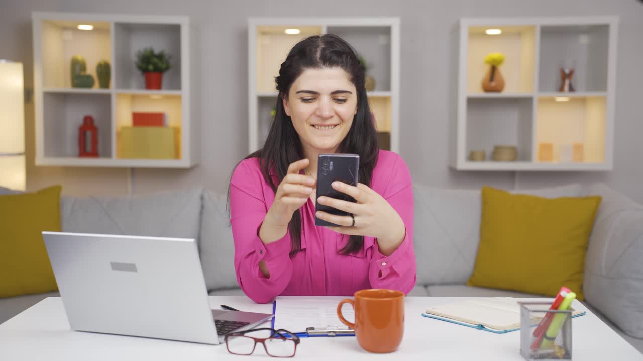 una mujer que trabaja en una oficina en casa recibe buenas noticias por teléfono.
