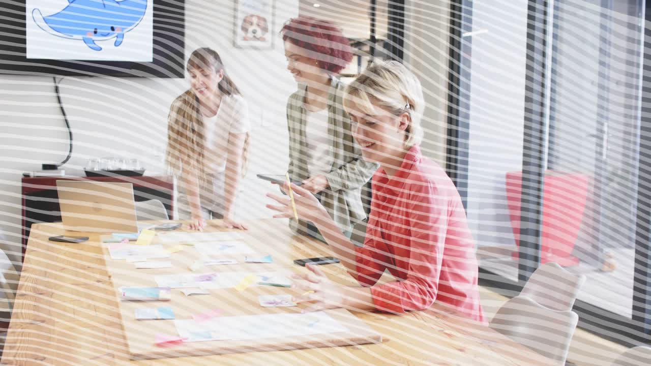 Three women meeting around long table, spotting tablet and rearranging sticky notes for design