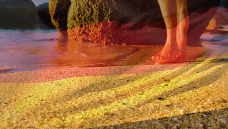 Animation of german flag over legs of caucasian woman walking in shallow sea on sunny beach