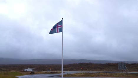 the flag of iceland flying in the wind on a flagpole by a country road