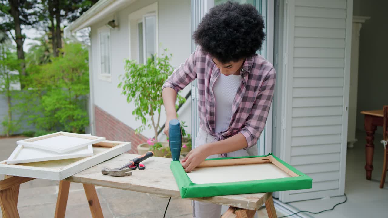 Donna afroamericana fissa del tessuto verde con una cucitrice alla cornice di una porta per decorazione, controllando la tensione.
