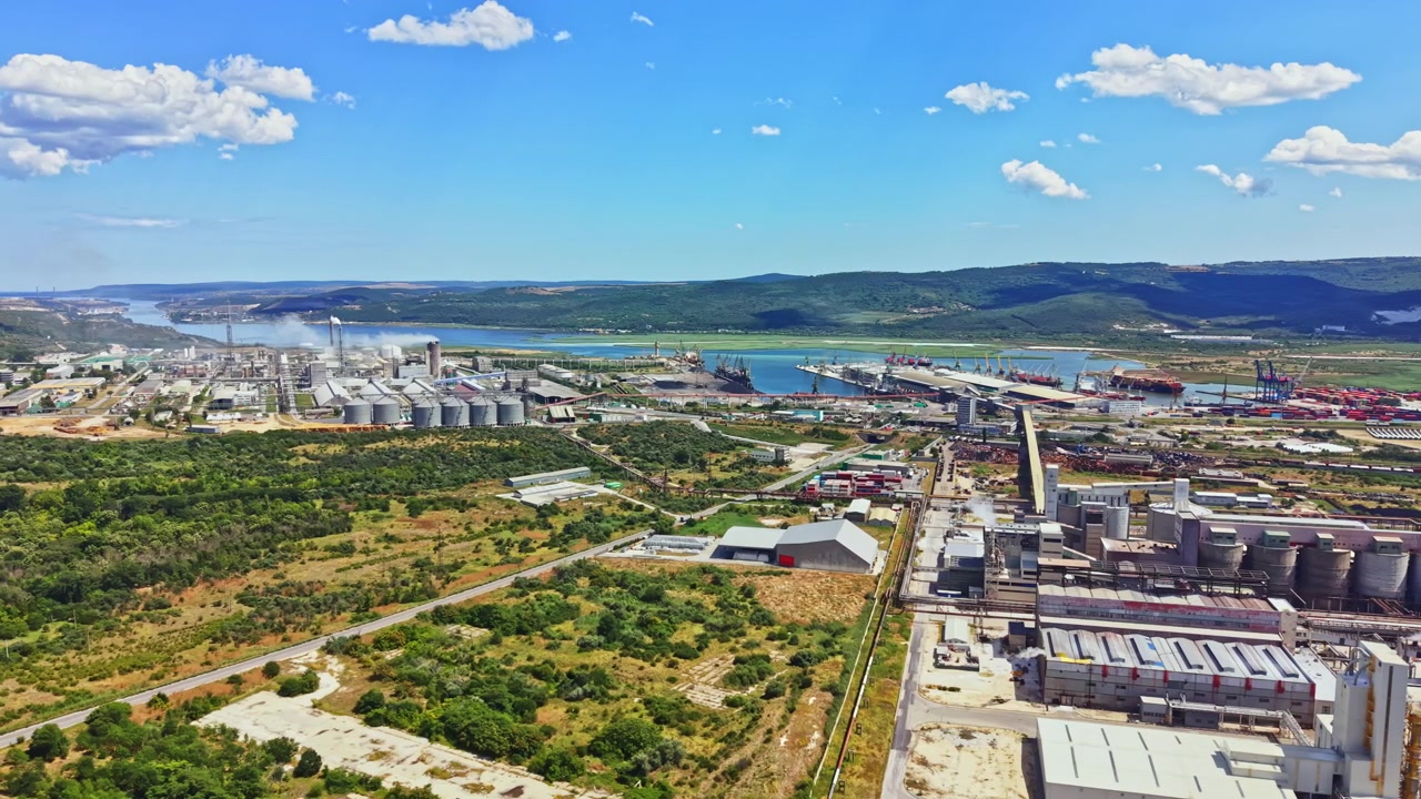 Vista di un'area industriale vicino al fiume con fabbriche e serbatoi di stoccaggio sotto un cielo blu con nuvole