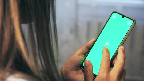A girl with brown hair holds a phone in her hands with a green background. Back view. A woman's hand holds a mobile phone on the screen of which is a chroma key. A woman is scrolling on her phone.