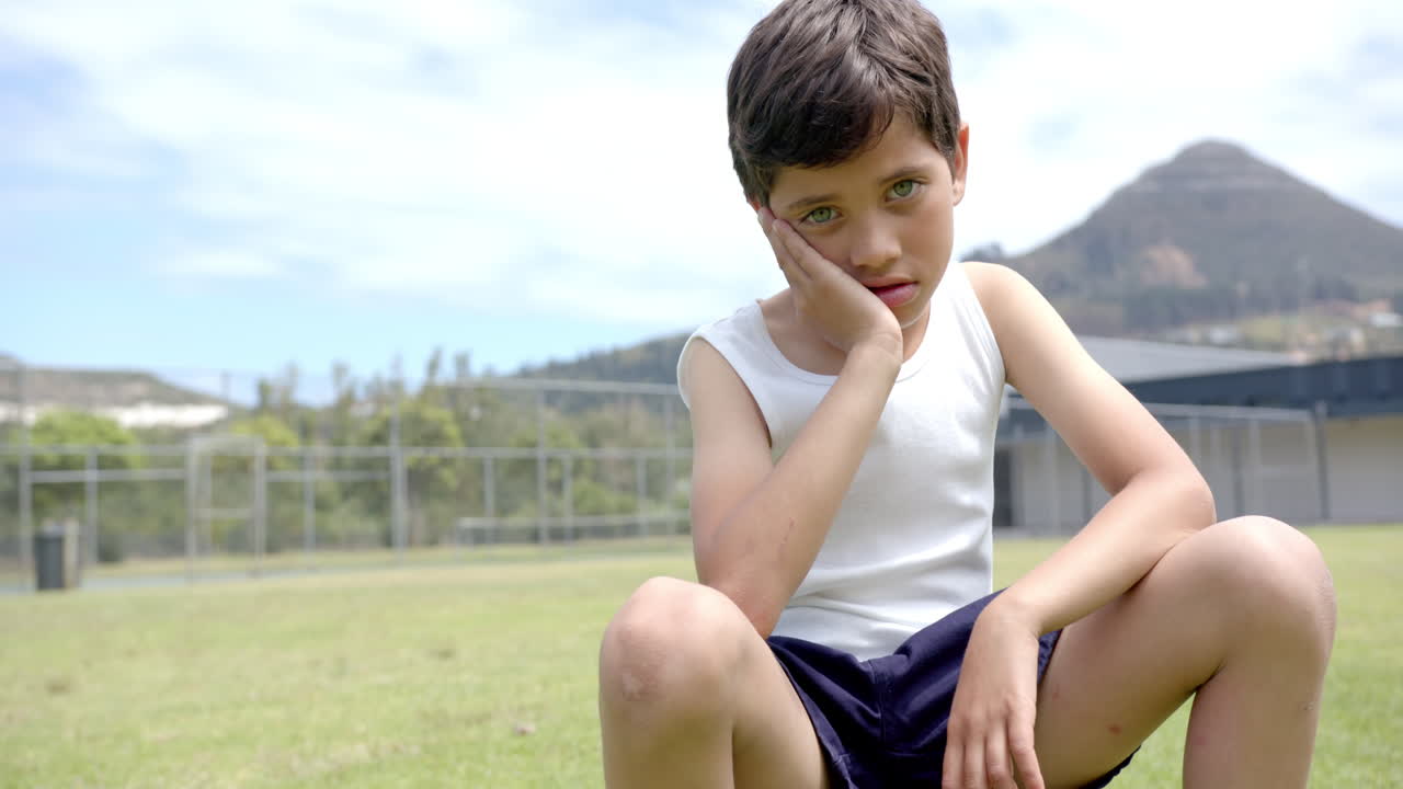 In school, child sitting on grass field, looking thoughtful and resting head on hand, copy space