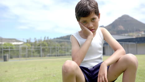 in school, child sitting on grass field, looking thoughtful and resting head on hand, copy space