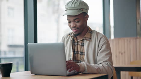 happy black man typing on laptop in coffee shop