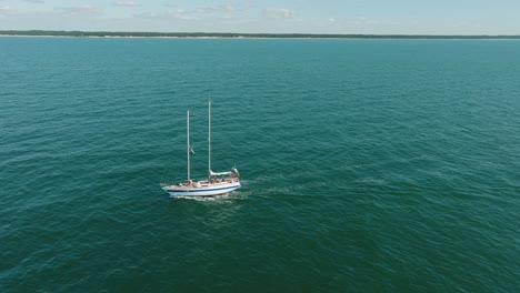 Aerial-establishing-view-of-a-white-sailboat-in-the-calm-Batltic-sea,-white-sailing-yacht-in-the-middle-of-the-boundless-sea,-sunny-summer-day,-wide-done-shot