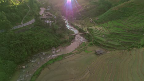 vista aérea de un arroyo de agua con un campo de arroz a la derecha y la carretera a la izquierda, un rayo de sol brillando y un dron alejándose revelando un hermoso paisaje