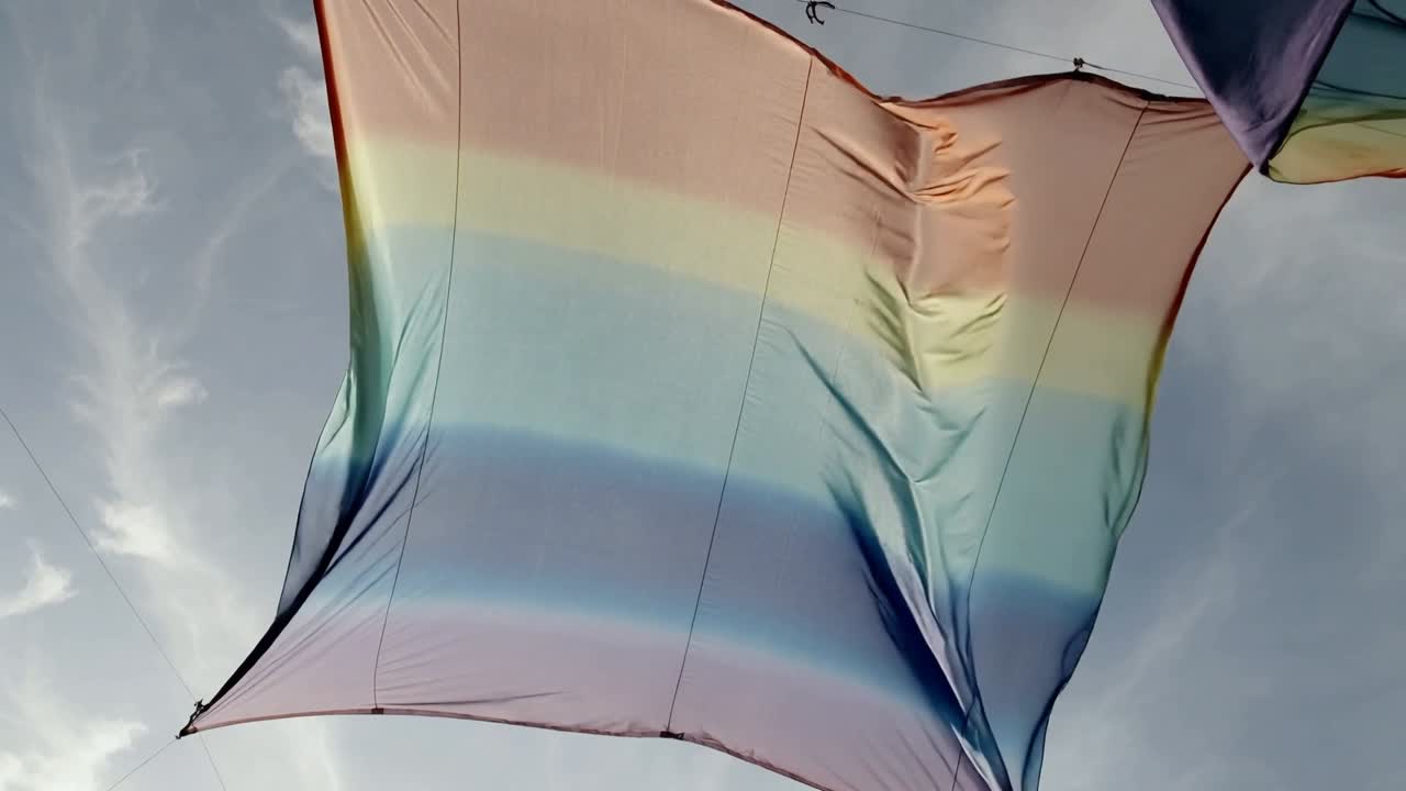 Brezza che solleva un grande pannello arcobaleno, facendolo gonfiare e appiattire all'aperto con clip metalliche e un secondo pannello