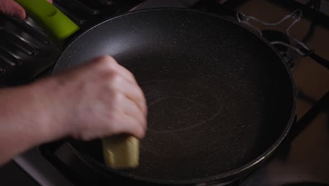 close-up view of a hand that is applying butter to a frying pan - steady shot