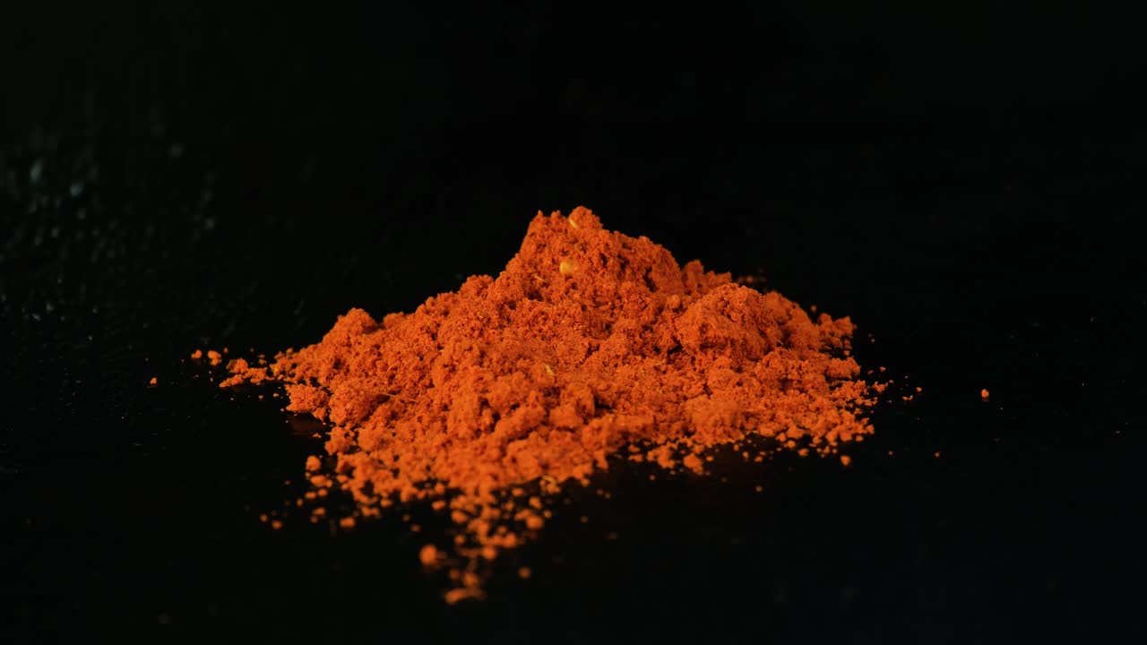 Man's hand placing whole red chili on top red chili pepper powder on the black table surface and background