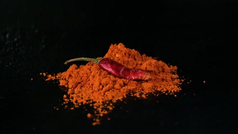 Man's-hand-placing-whole-red-chili-on-top-red-chili-pepper-powder-on-the-black-table-surface-and-background