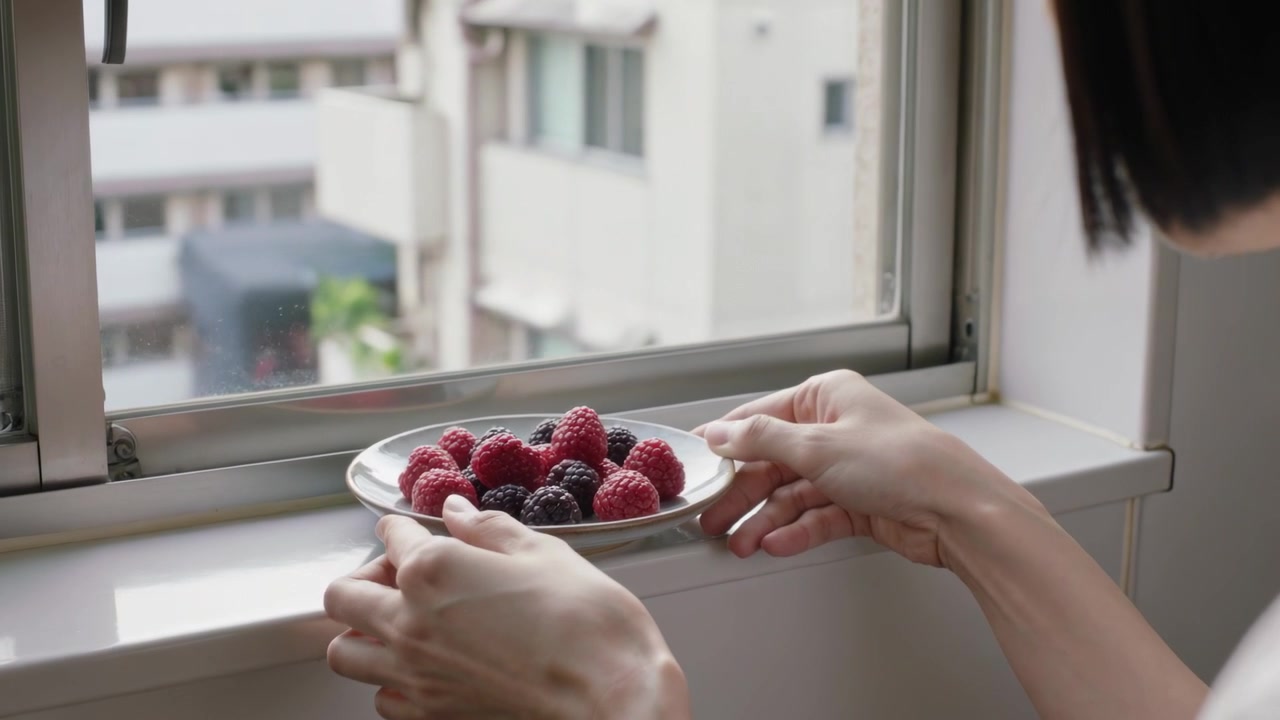 Placing woman in grey apron seeing daylight and lowering plate of berries onto windowsill