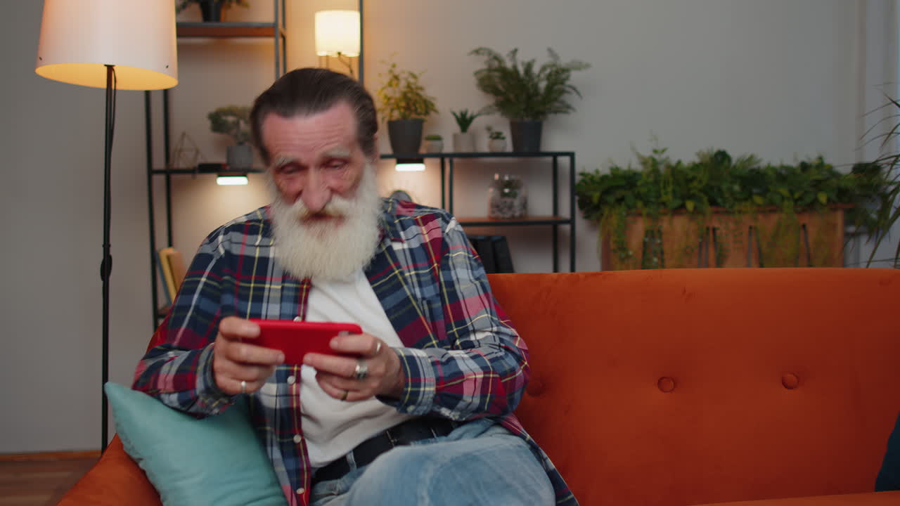 Preoccupato divertente anziano vecchio nonno uomo che gioca a corse online videogiochi sullo smartphone a casa