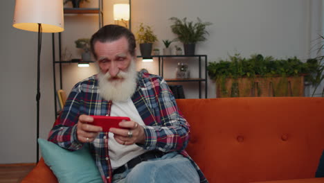 Worried-funny-senior-old-grandfather-man-playing-racing-online-video-games-on-smartphone-at-home