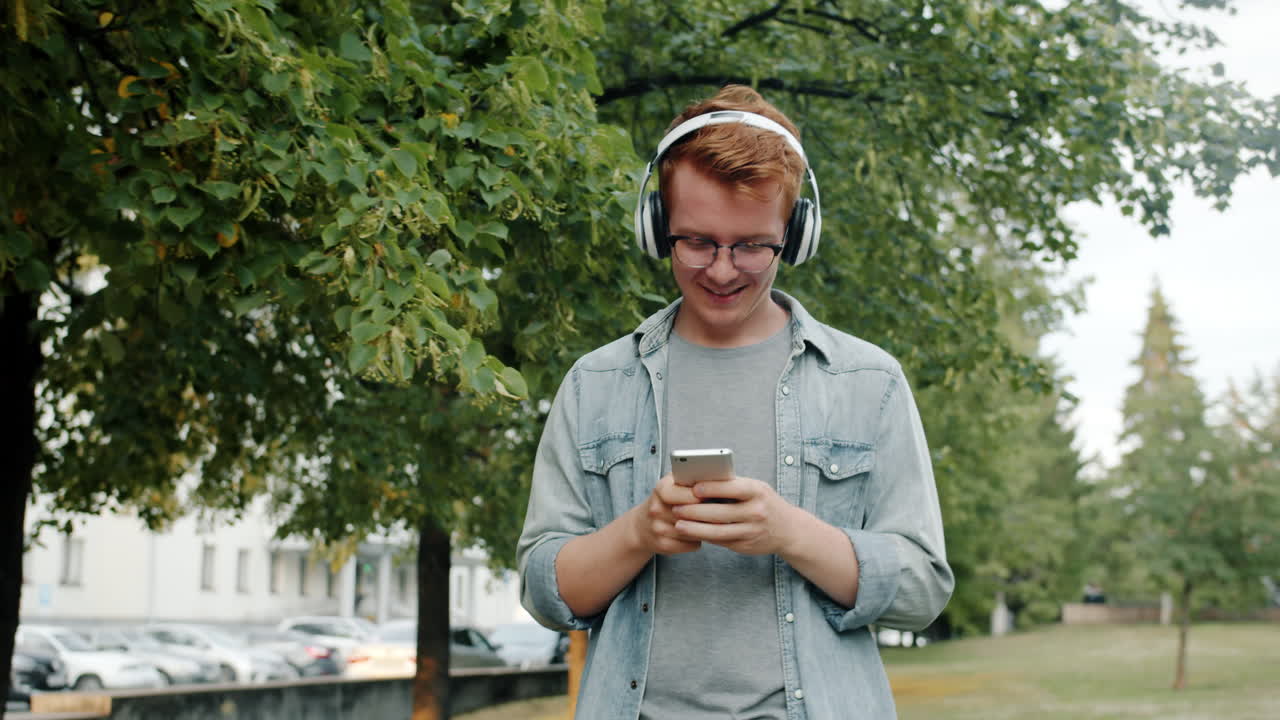 Young Man Listening to Music and Using Phone in a Park