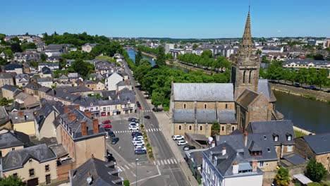 drone flies forward along street by notre-dame d’avesnières basilica with mayenne river and houses, low traffic. france