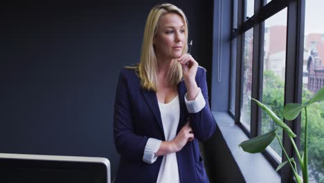 Caucasian-businesswoman-standing-looking-through-a-window-in-modern-office