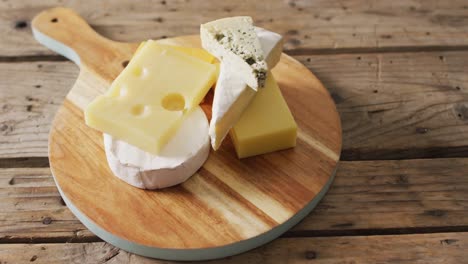 video of assorted hard and soft cheeses on wooden chopping board and rustic table, with copy space