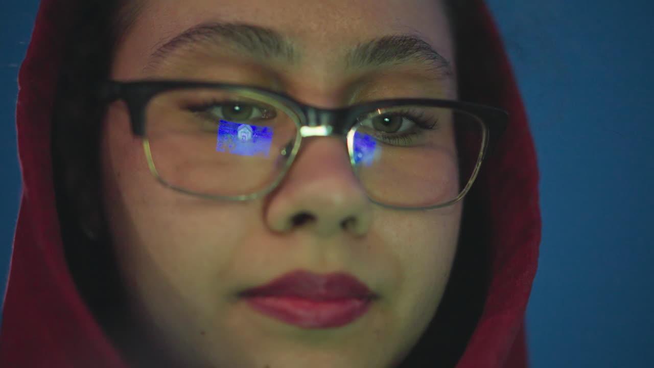 Selfassured Female Portrait, Woman With Glasses And Focused Expression, Confident Woman Wearing Red Hood And Looking Directly, Steadyeyed Woman In Blue Lighting With Determined And Peaceful Demeanor