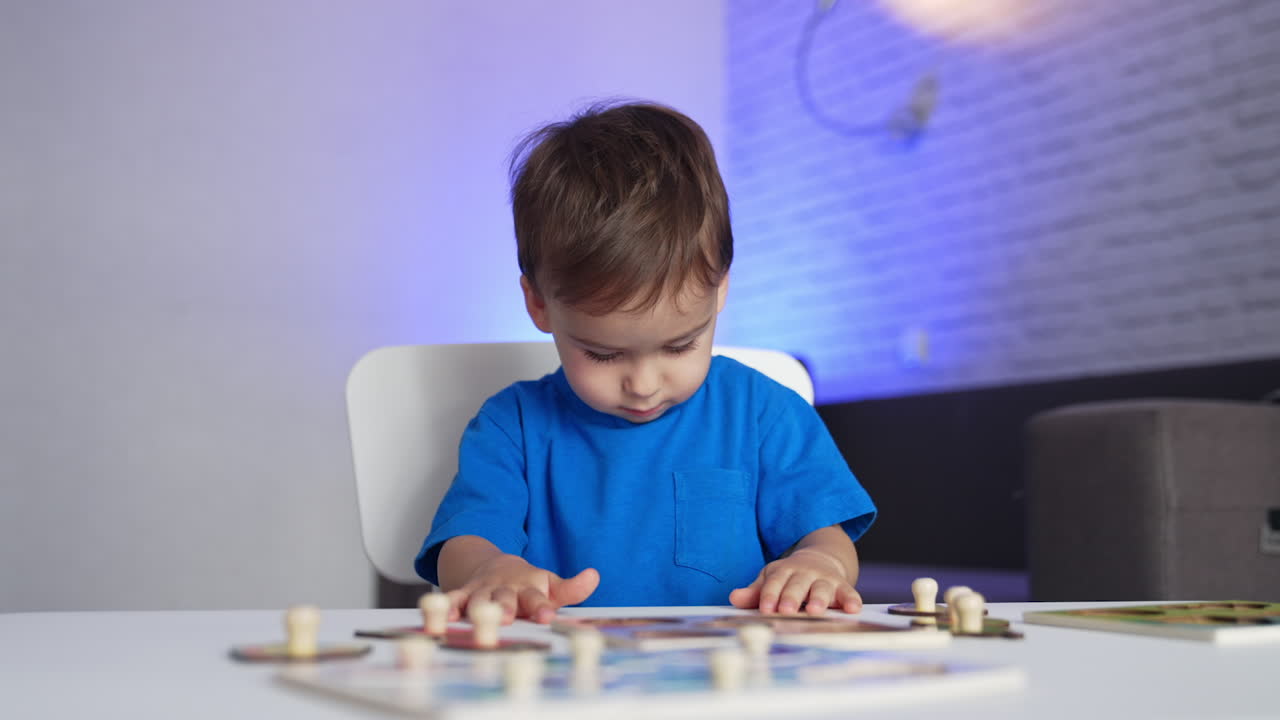 Charming little toddler in blue shirt playing games at desk. Calm baby boy stands up and walks away.