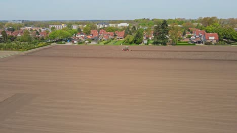 Stunning-aerial-of-tractor-plowing-a-plot-of-empty-land-at-the-edge-of-a-small-town