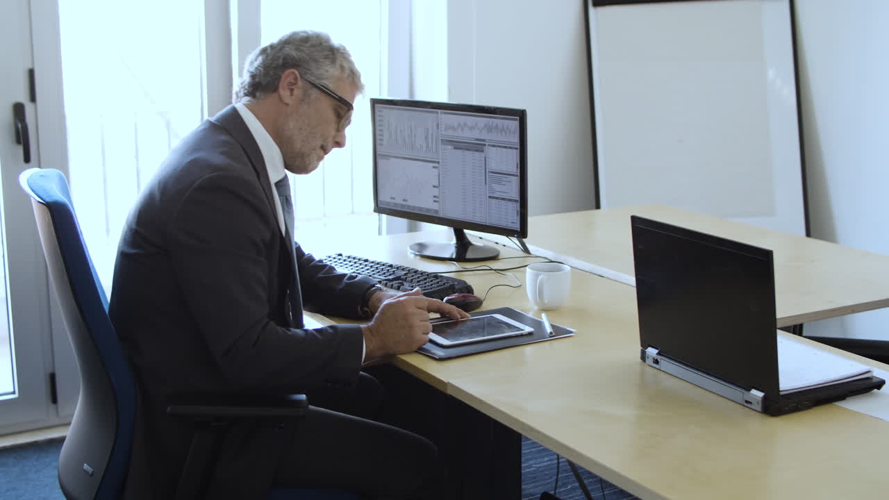 Focused grey haired experienced investor using computer and tablet