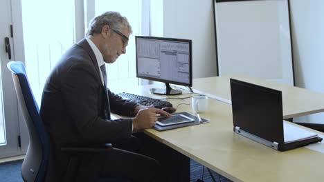 focused grey haired experienced investor using computer and tablet