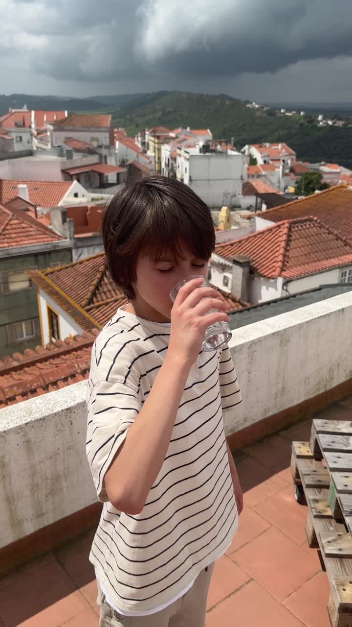 Boy Drinking Water on a Rooftop with City View