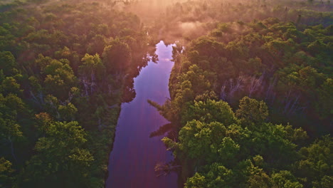 drone shot flying up foggy manistee river in the upper peninsula of michigan at sunrise with the fantastic colors of dawn