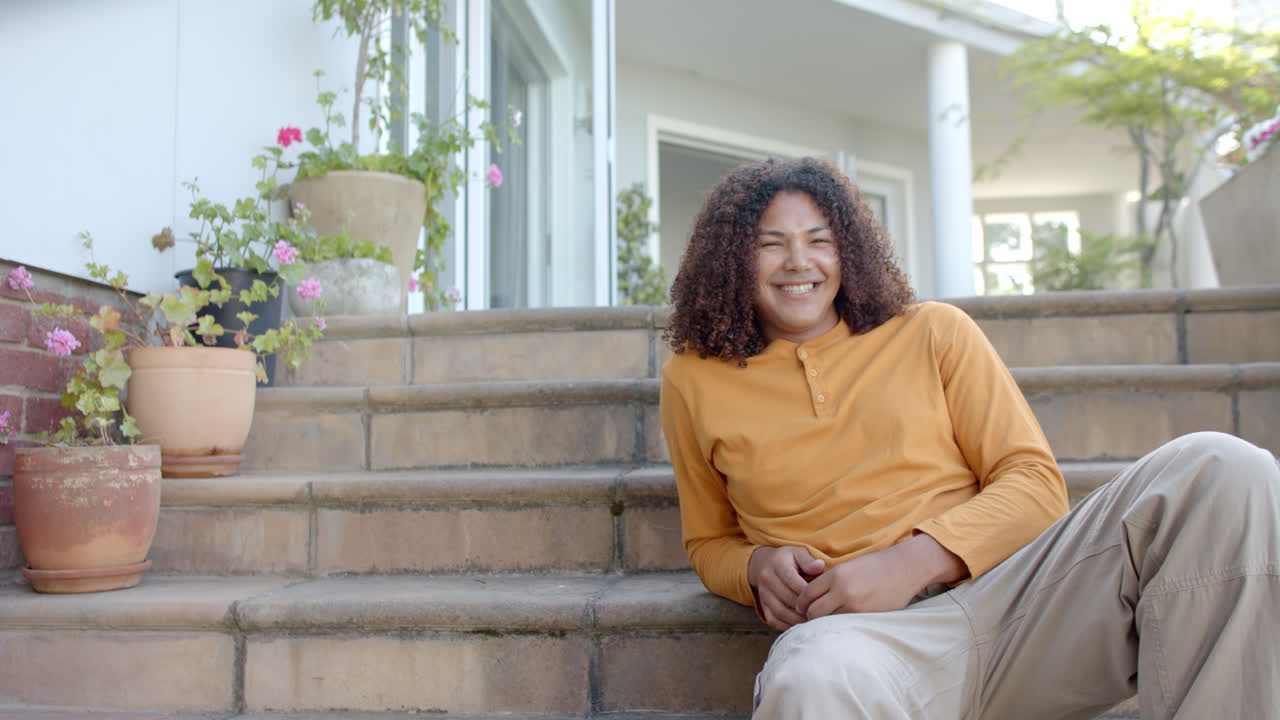 retrato de un hombre feliz de dos razas con cabello largo sentado en los escalones del jardín, espacio de copia, cámara lenta