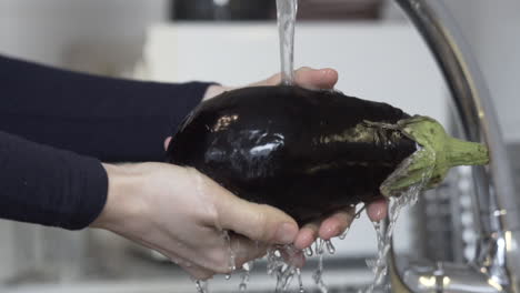 toma cercana en cámara lenta mientras se lava una berenjena en el fregadero con agua