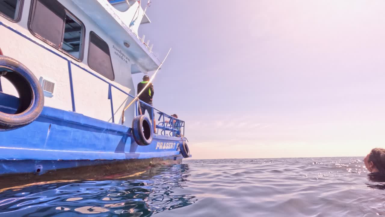 Underwater to surface view of swimmers approaching anchored dive boat in bright tropical sunlight