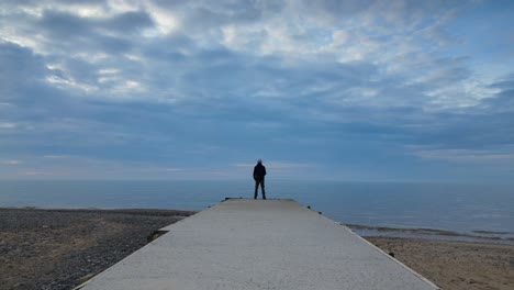 Slow-motion-man-staring-out-to-sea-at-the-end-of-a-jetty-at-dusk-on-Fleetwood-Beach-Lancashire-UK