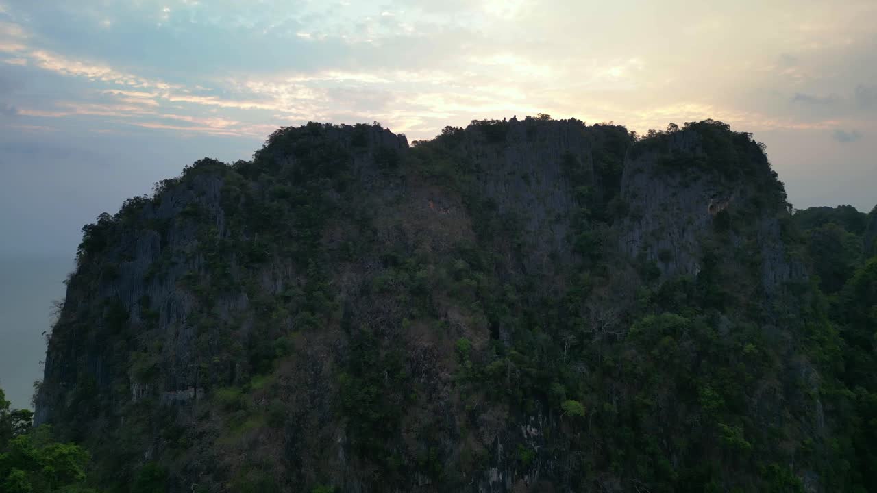 limestone cliffs and lush tropical jungle of Railay Beach, Krabi, Thailand, at dusk, creating a dramatic and serene landscape. overflight flyover drone