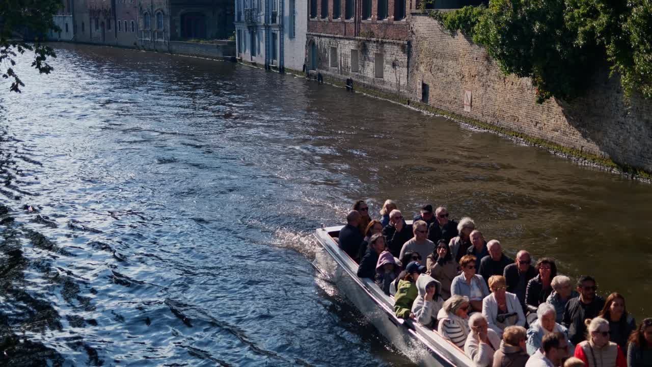 Tourist boats cruise along a scenic canal in historic Bruges, Belgium on a sunny day
