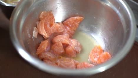 chef adding a spoonful of limon or lemon on a freshly cut raw salmon in a stainless steel bowl in preparation for ceviche recipe