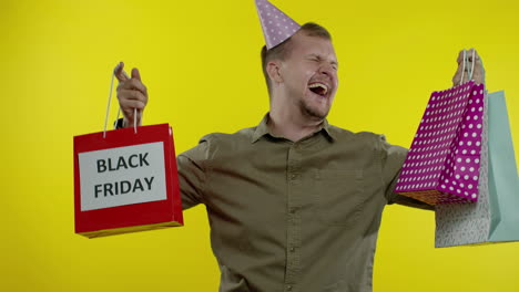 hombre sonriente mostrando la inscripción de black friday en las bolsas de compras, celebrando, regocijándose de buenos descuentos